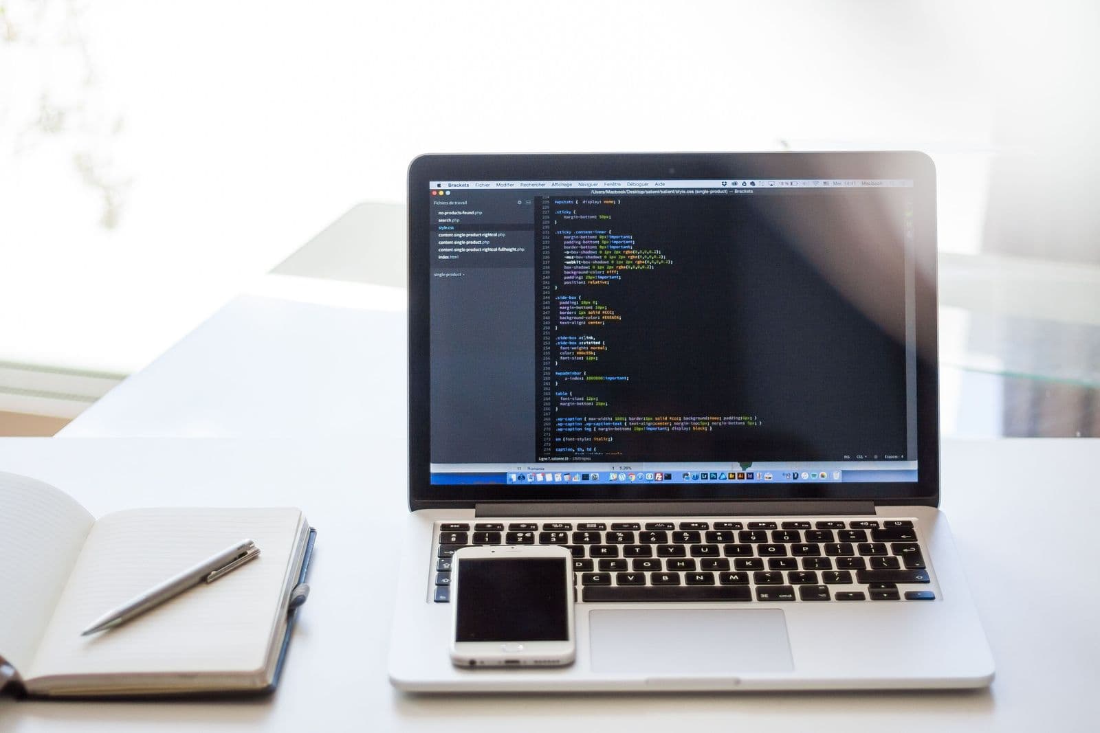 Ordinateur portable ouvert sur du code, carnet et téléphone
